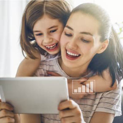 Two sisters laughing and smiling at a tablet the older sister is holding
