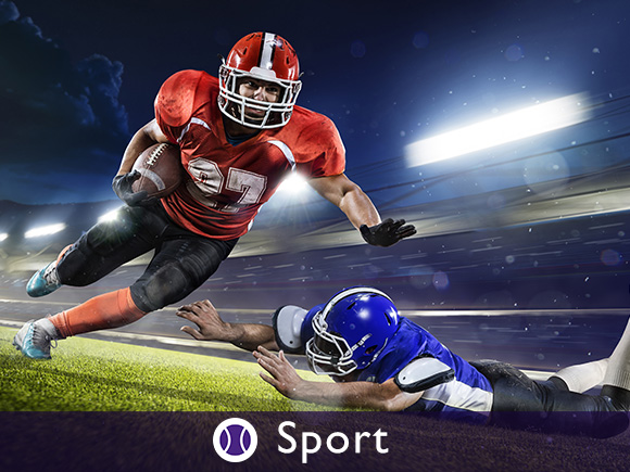 A football player in red running with the ball past a blue player who missed the tackle