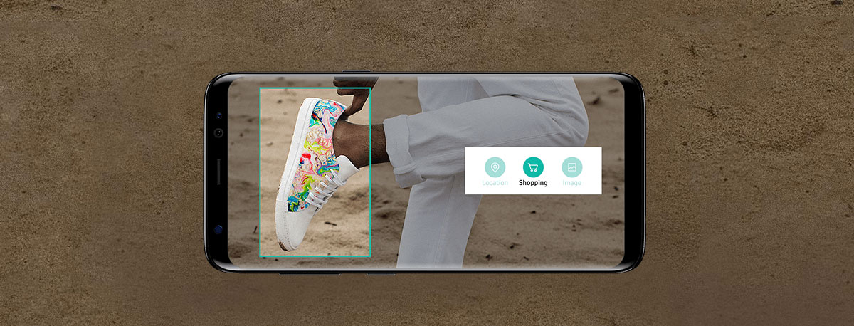 The Samsung Galaxy S8 phone facing forward, lying horizontally showing a woman tucking in her shoe back while she stands on sand