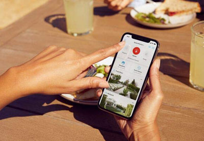 An iPhone held by two hands, with screen showing camera feeds