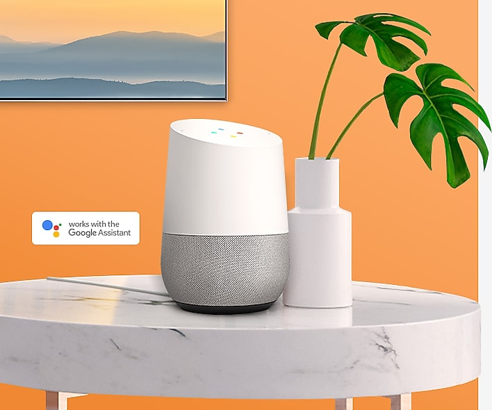 SAMSUNG Q80R mounted on an orange wall, with the google assistant on a marble table next to a potted plant