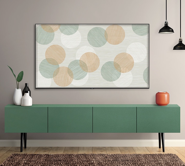 SAMSUNG Q80R display mounted on a wall with fabric polka dots on screen. The tv is a bove a green cabinet