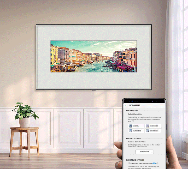 SAMSUNG Q80R display mounted showing an art painting of a river town going in and out of contrast by way of a hand with a smartphone controlling it via app