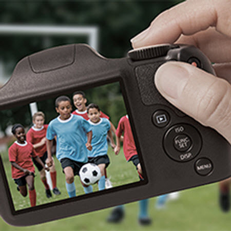 a hand holding a camera showing kids palying football