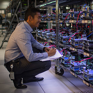 A male squatting in front of wheeled storage racks, full of drives