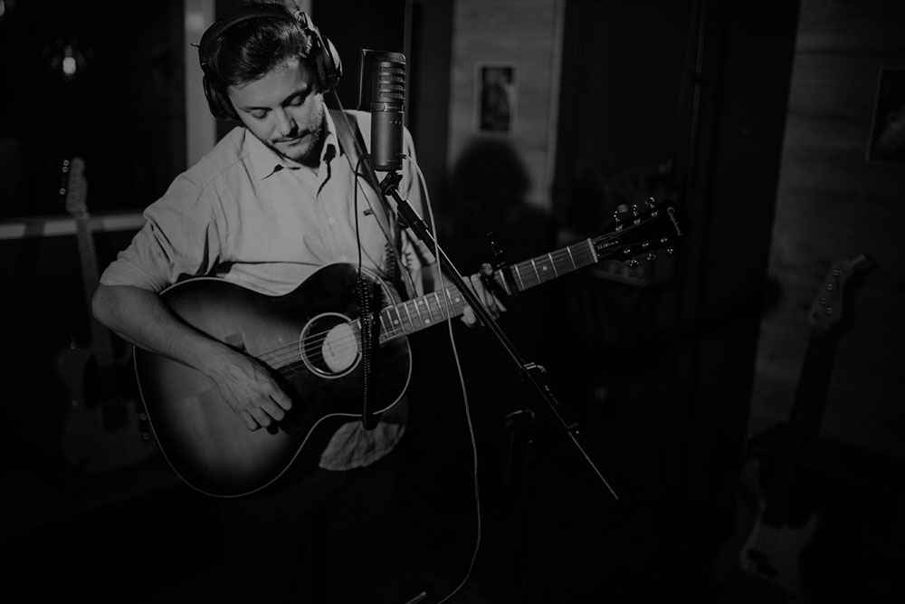 A guitarist in the studio booth in front of a mic