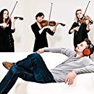 A Man Wearing Red Audio-Technica Headphones, Lounging on a Couch while Three Female Violinists Play Behind Him