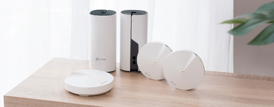 TP-Link Deco devices on a wooden table by a white-curtained window during the day