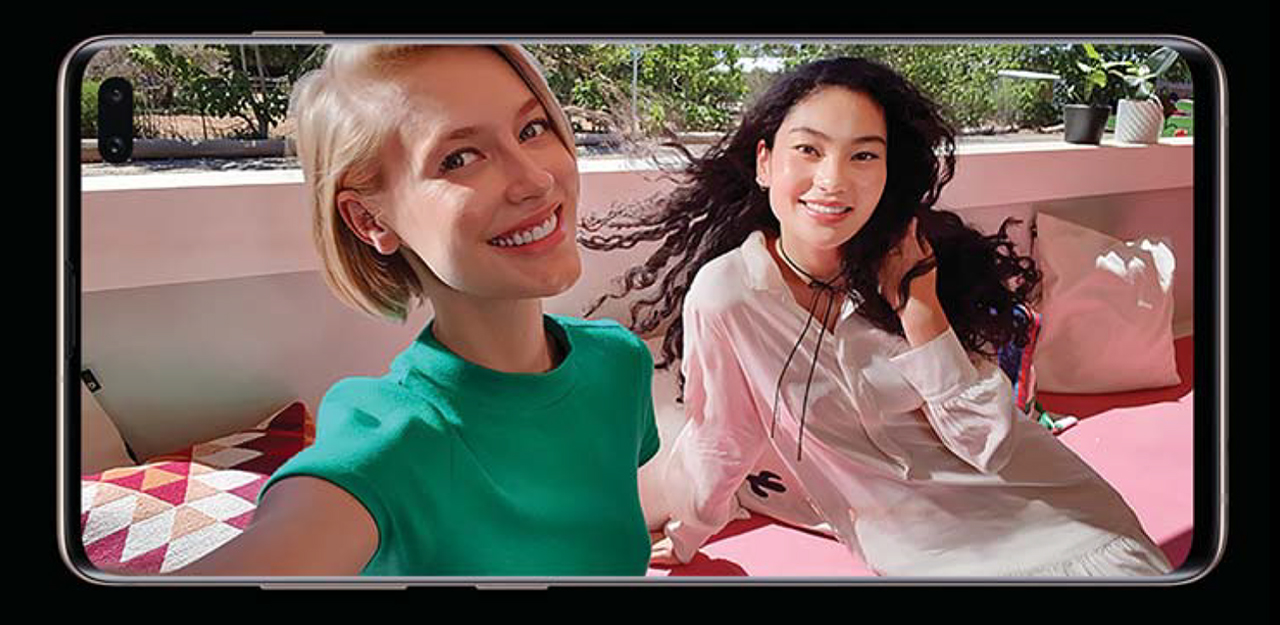 A Samsung Galaxy S10 sitting horizontally on its side showing two young women taking a selfie next to each other in an outdoor cabana