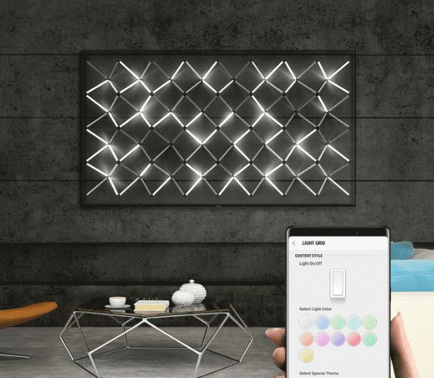 A wall-mounted Samsung Q70R display showing a a modern light art installation. At the forefront is a hand using a smartphone that's controlling the content on the TV.