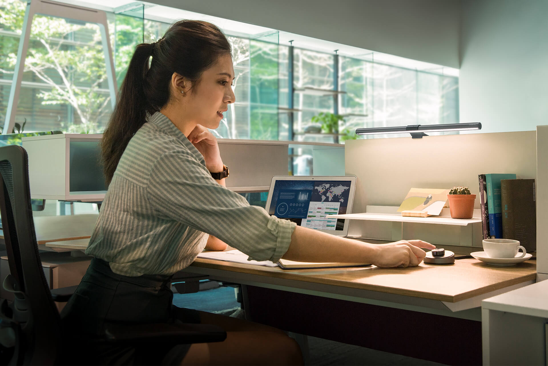 A female office worker at her desk utilizing the BenQ ScreenBar Plus's desktop dial with her right hand