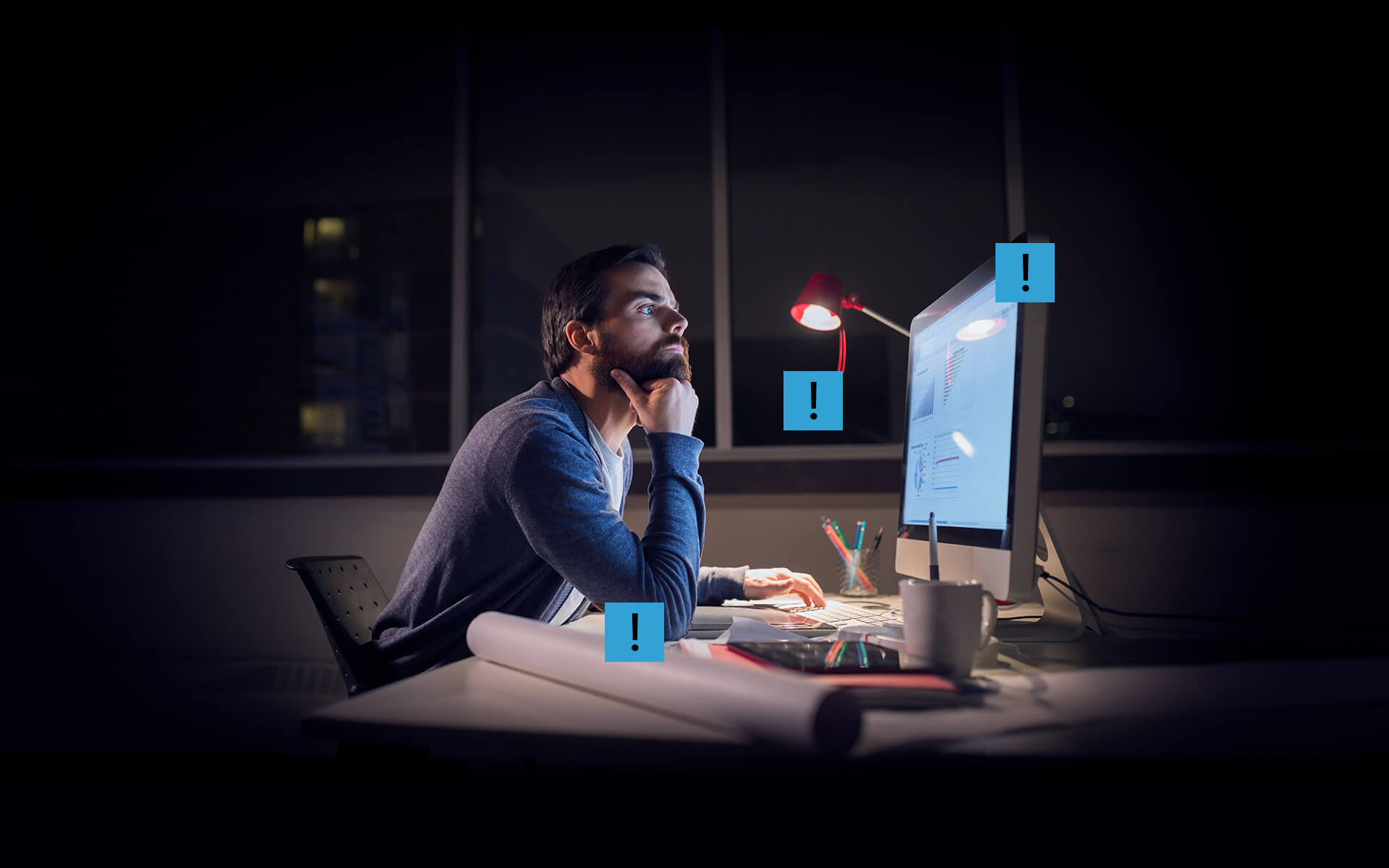 A man in front of his imac working at his desk at night