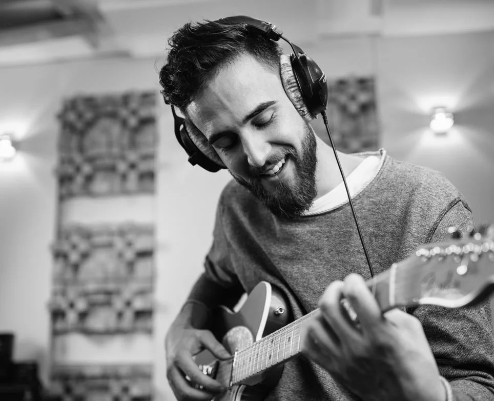 A man wearing a Beyerdynamic DT-770 PRO 250 Ohms Studio Over-Ear Headphones playing a guitar