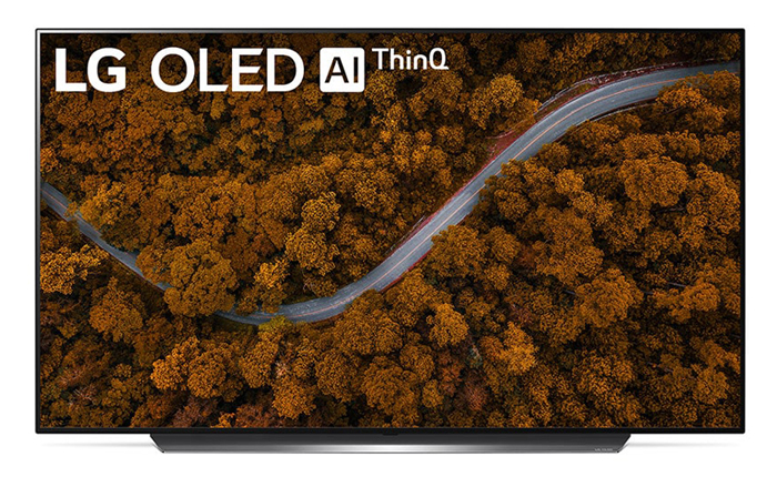 A TV is displaying a road cuting across a forest with orange trees. In the top left corner is text reading LG OLED AI ThinQ