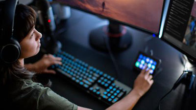 A woman at her streaming desk, wearing a headset and touching her Elgato touch screen deck