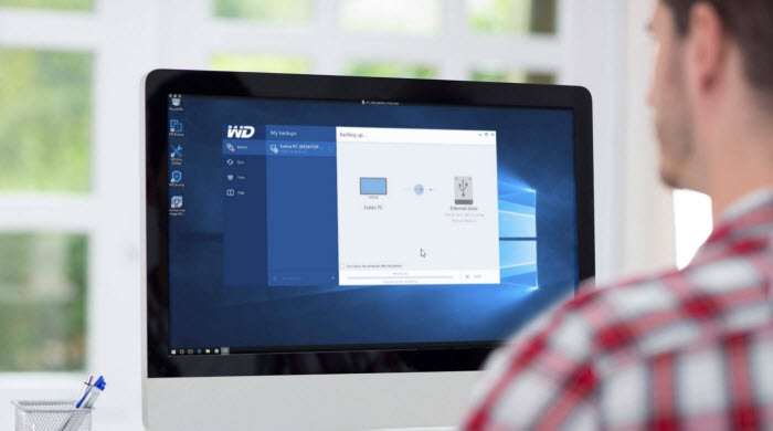 A man using an all-in-one desktop PC with Acronis True Image WD Edition software on screen