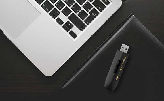 Team Group Flash Drive on a Black Notebook Next to an Open Laptop