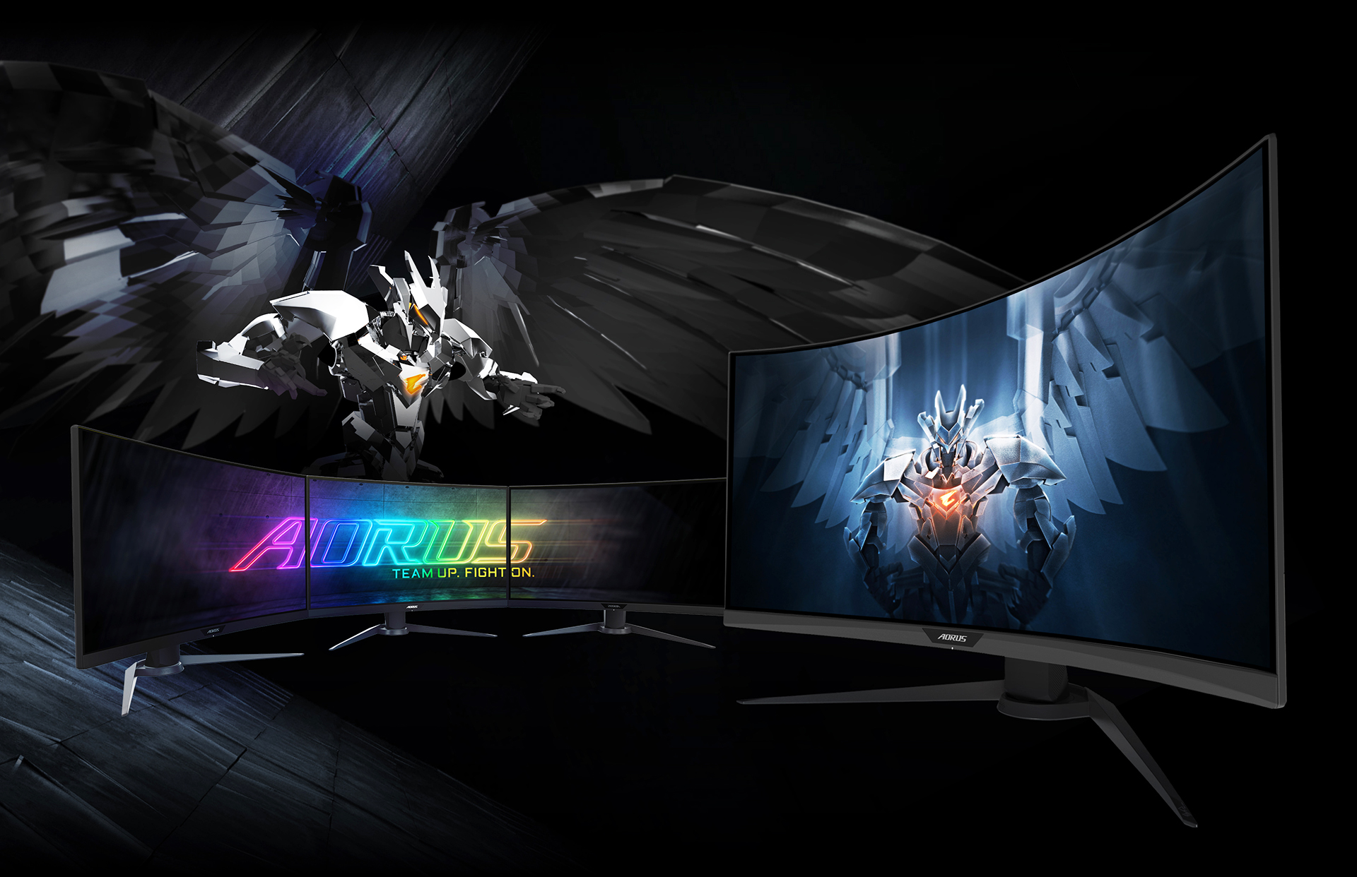 A Set of Three AORUS Monitors Side by Side, Forming a Connected Display of the AORUS Team Up, Fight On Logo. Behind the Monitor Is the Aorus CGI Character, and to the Right of All This Is Another Monitor Angled to the Left with Graphic Artwork of the Aorus Character