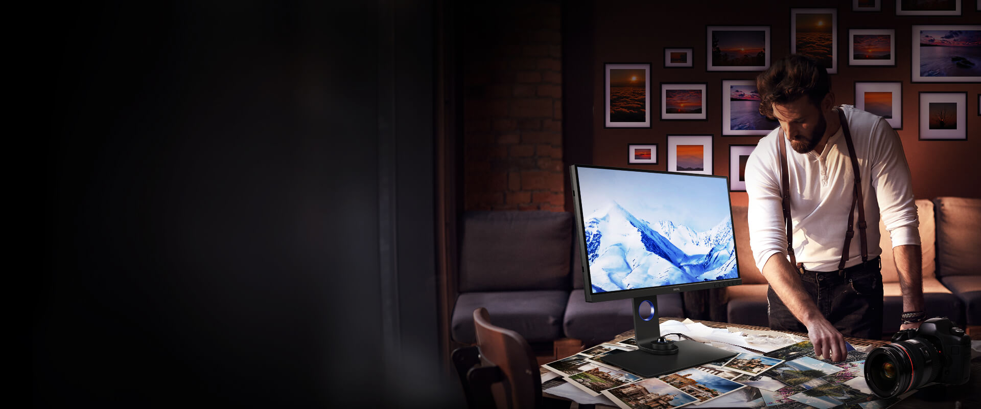 A male photographer looking at photos on his desk next to the BenQ SW270C monitor with an image of snow covered mountains