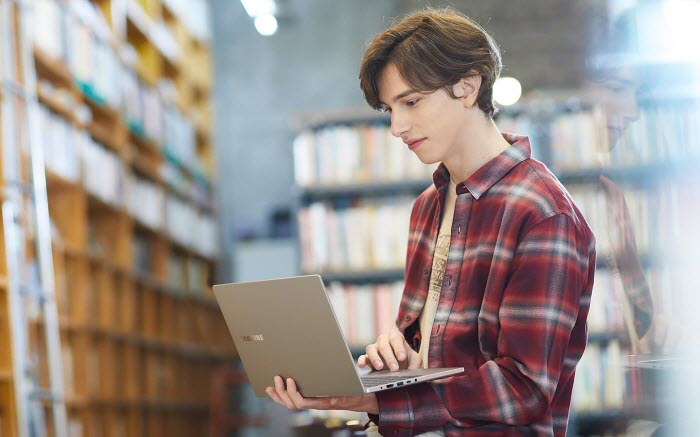 a young man holding Samsung Notebook 7 in the library