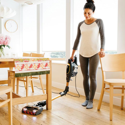 A woman utilizing the multiflex function as she has the vacuum completely under a table on a hardware floor