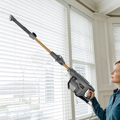 Woman using the vacuums extender to vacuum the individual shades of her window blinds