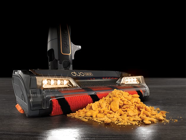 closeup of the shark HV392 pickup up crumbled cheese cracker snacks on a brown hardwood floor