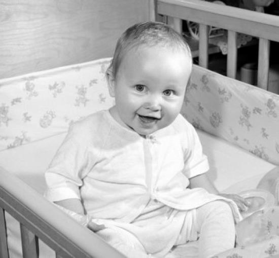 Portrait of cheerful baby sitting in cot Poster Print (18 x 24) 